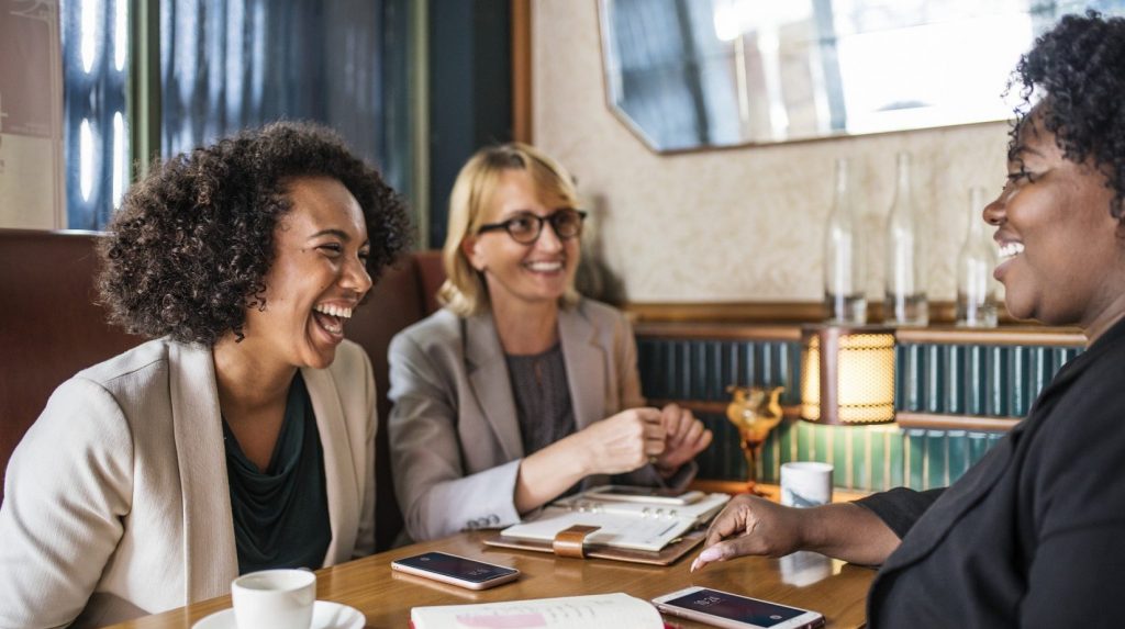 Drei Frauen lachen und unterhalten sich an einem Tisch
